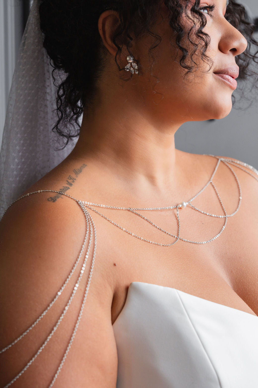 a woman is wearing a strapless wedding dress and a silver shoulder necklace with pearls that drapes over her arms like sleeves