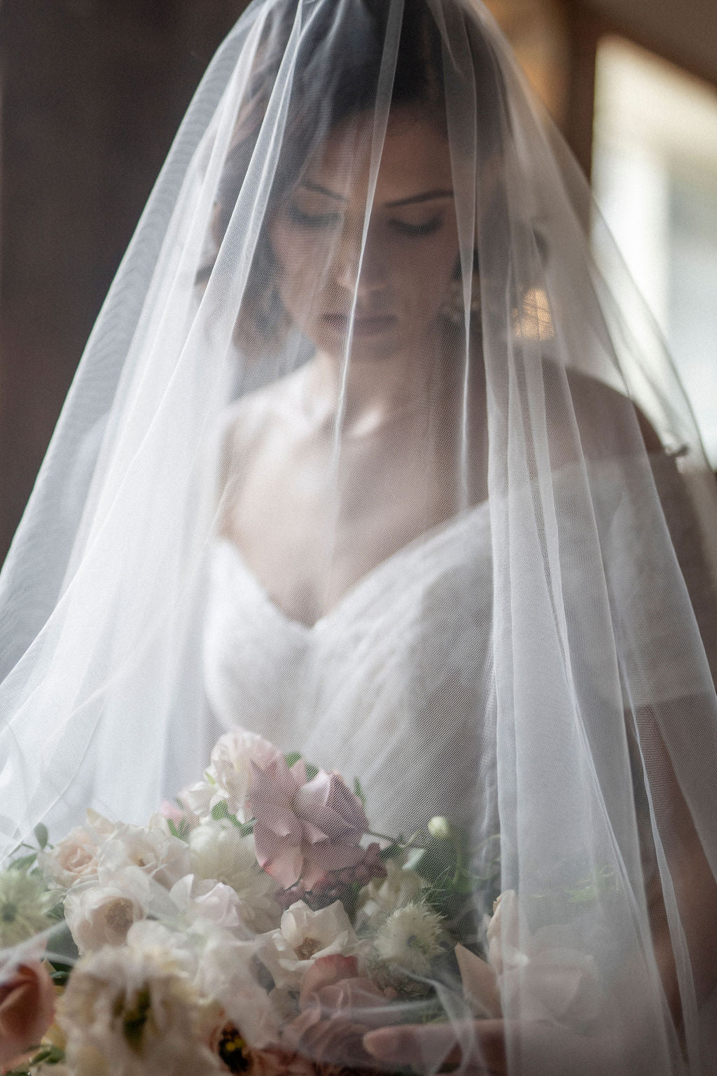  a woman is wearing a white off the shoulder vintage wedding dress with a sheer blusher wedding veil and holding a floral wedding veil