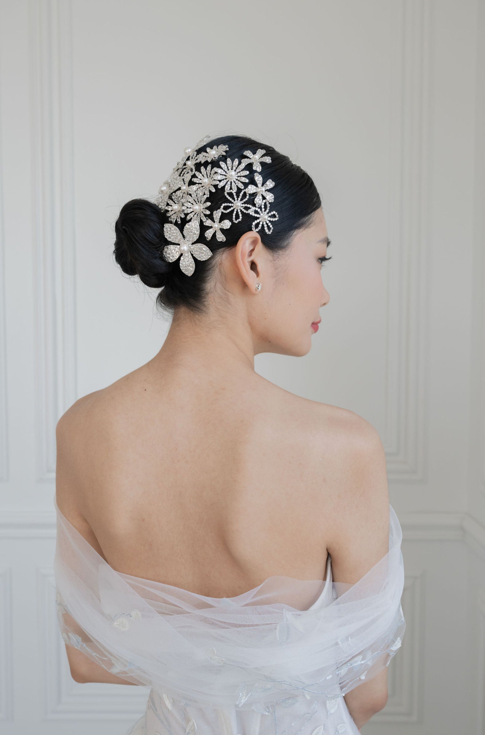 a woman is wearing an off the shoulder dress with a tulle shawl.  Her dark hair is in a slick bun and she is wearing multiple silver crystal hair combs in her hair