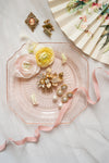 Decorative pink plate with jewelry and flowers on a light background