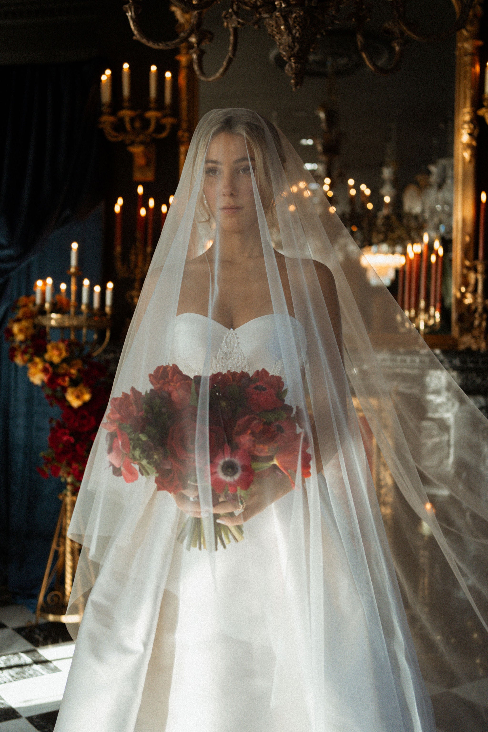 Woman in a wedding dress holding a bouquet in a grand, candlelit room.