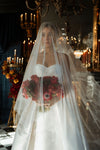 Woman in a wedding dress holding a bouquet in a grand, candlelit room.