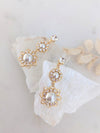 Gold and pearl earrings on a white stone surface