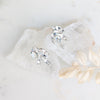 Pair of silver earrings with clear gemstones on a white fabric background