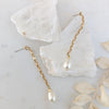 Gold chain earrings with pearl drops on a marble surface with leaves.