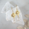Gold earrings with pearl drops on a white fabric background