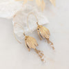 Gold leaf earrings with pearl-like beads on a white background