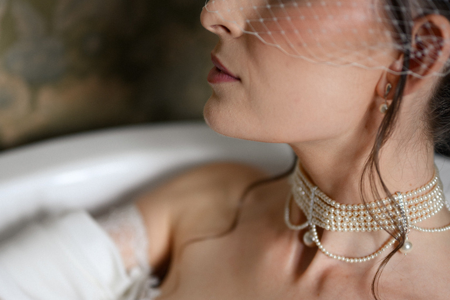 Close-up of a woman wearing a pearl choker and earrings with a blurred background