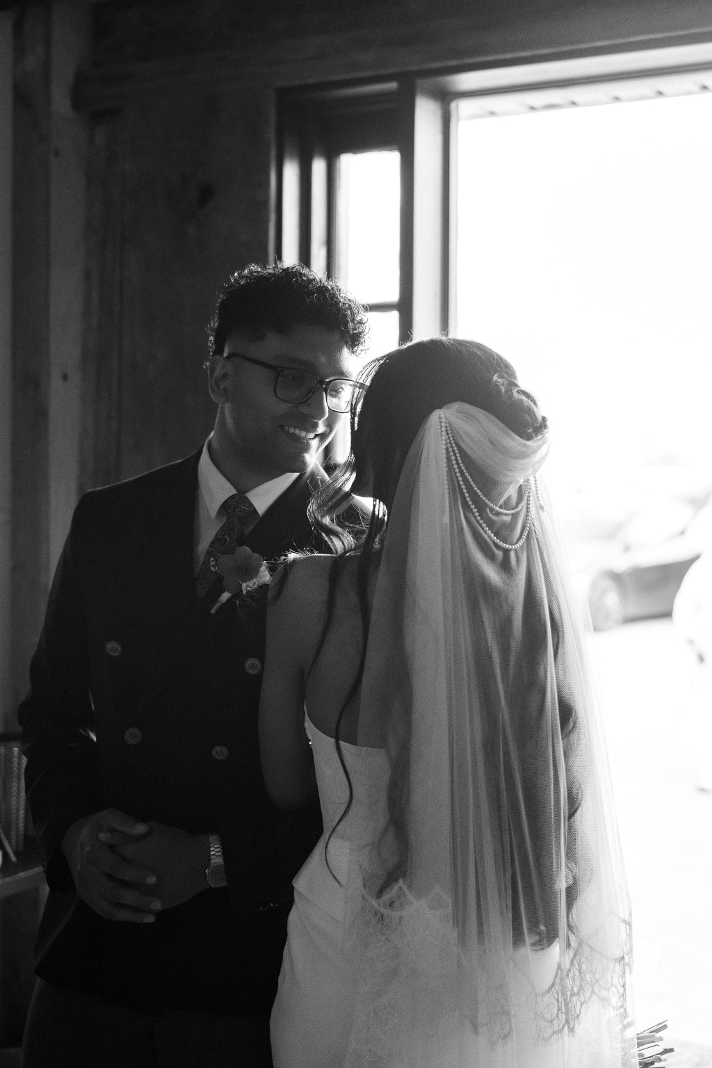 Black and white photo of a couple embracing indoors with a window in the background.