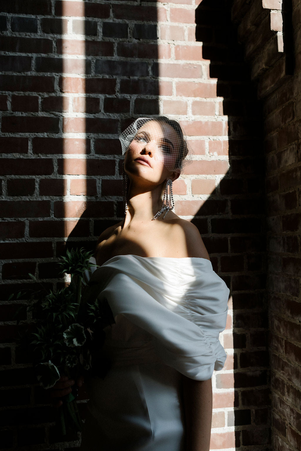Woman in a white dress standing against a brick wall with a veil