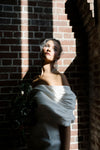 Woman in a white dress standing against a brick wall with a veil