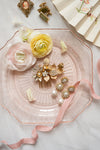 Decorative items including flowers, a comb, and jewelry on a pink plate with a fan in the background.
