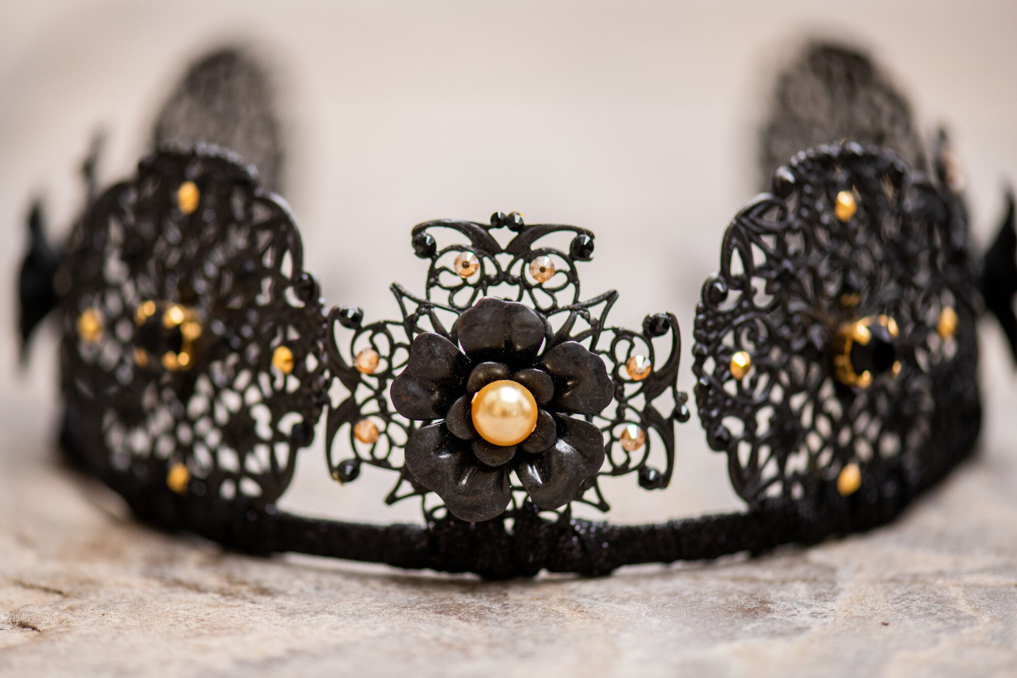 Black lace headband with floral design and pearl center on a neutral background
