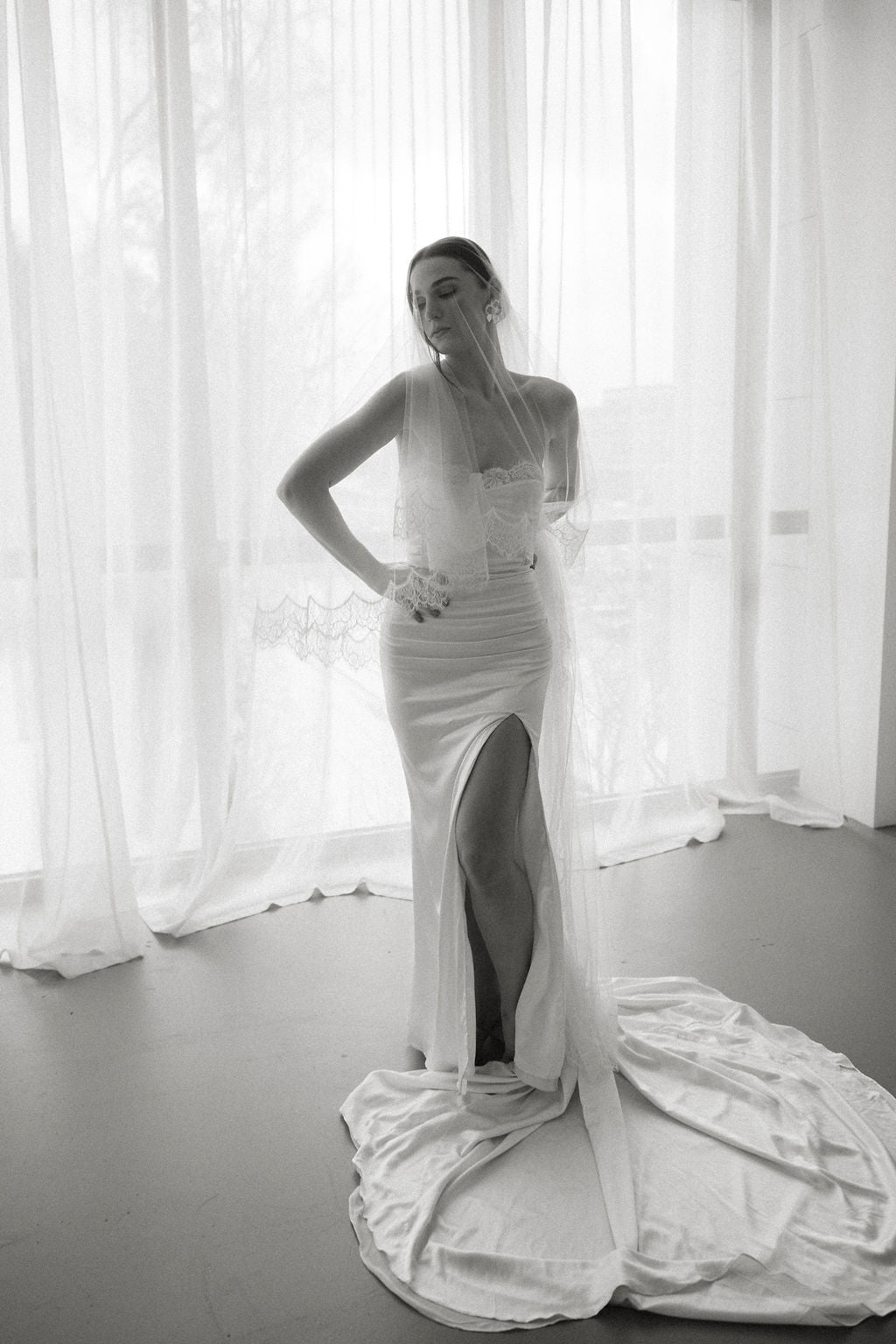 Woman in a white wedding dress standing in front of sheer curtains.