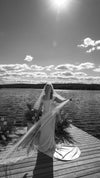 Woman in a wedding dress with a long veil standing on a dock by a lake.