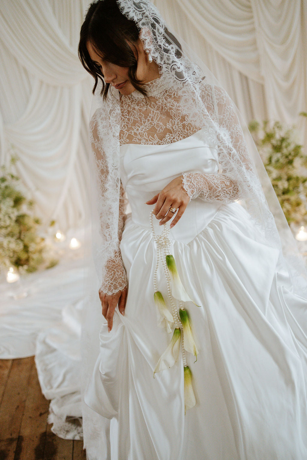 Woman in a white wedding dress with a lace veil holding flowers in a decorated indoor setting.
