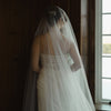 Bride in a white wedding dress with a long veil standing by a window.