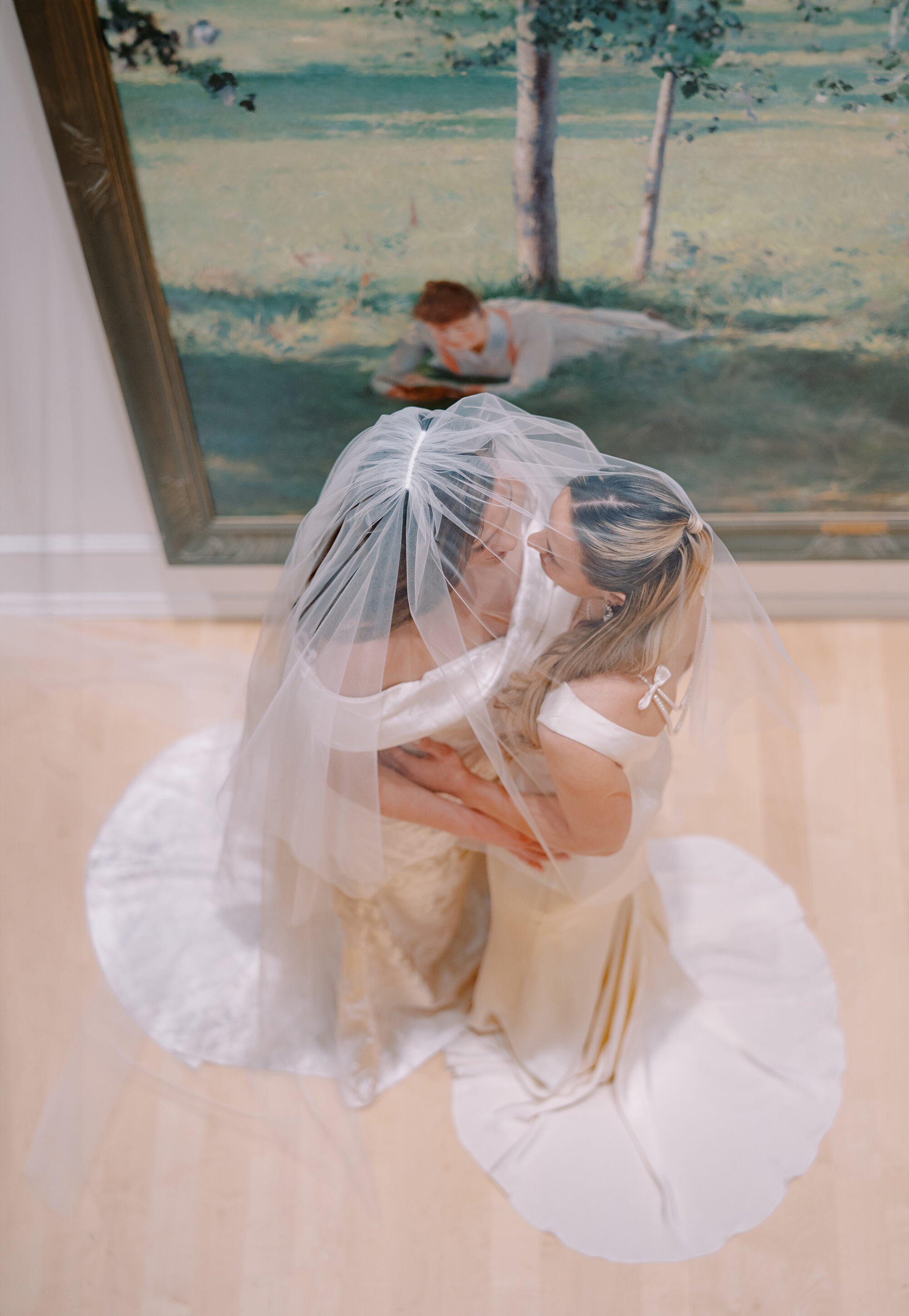 Person wearing a white dress with a sheer overlay in front of a painting