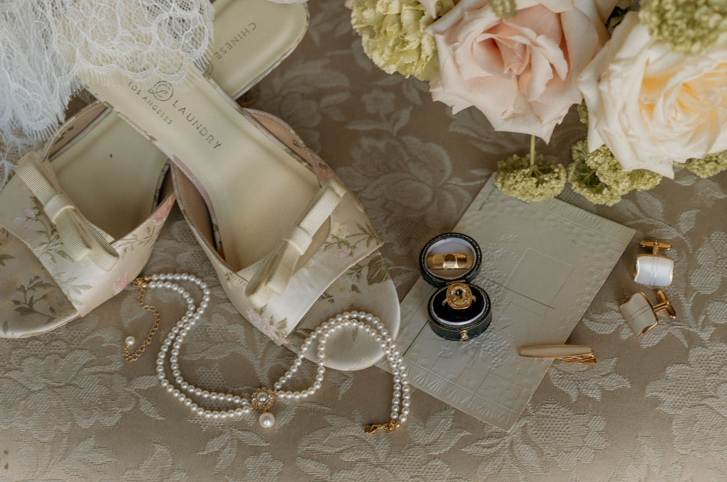 Wedding shoes, necklace, pearls, ring, and flowers on a lace surface