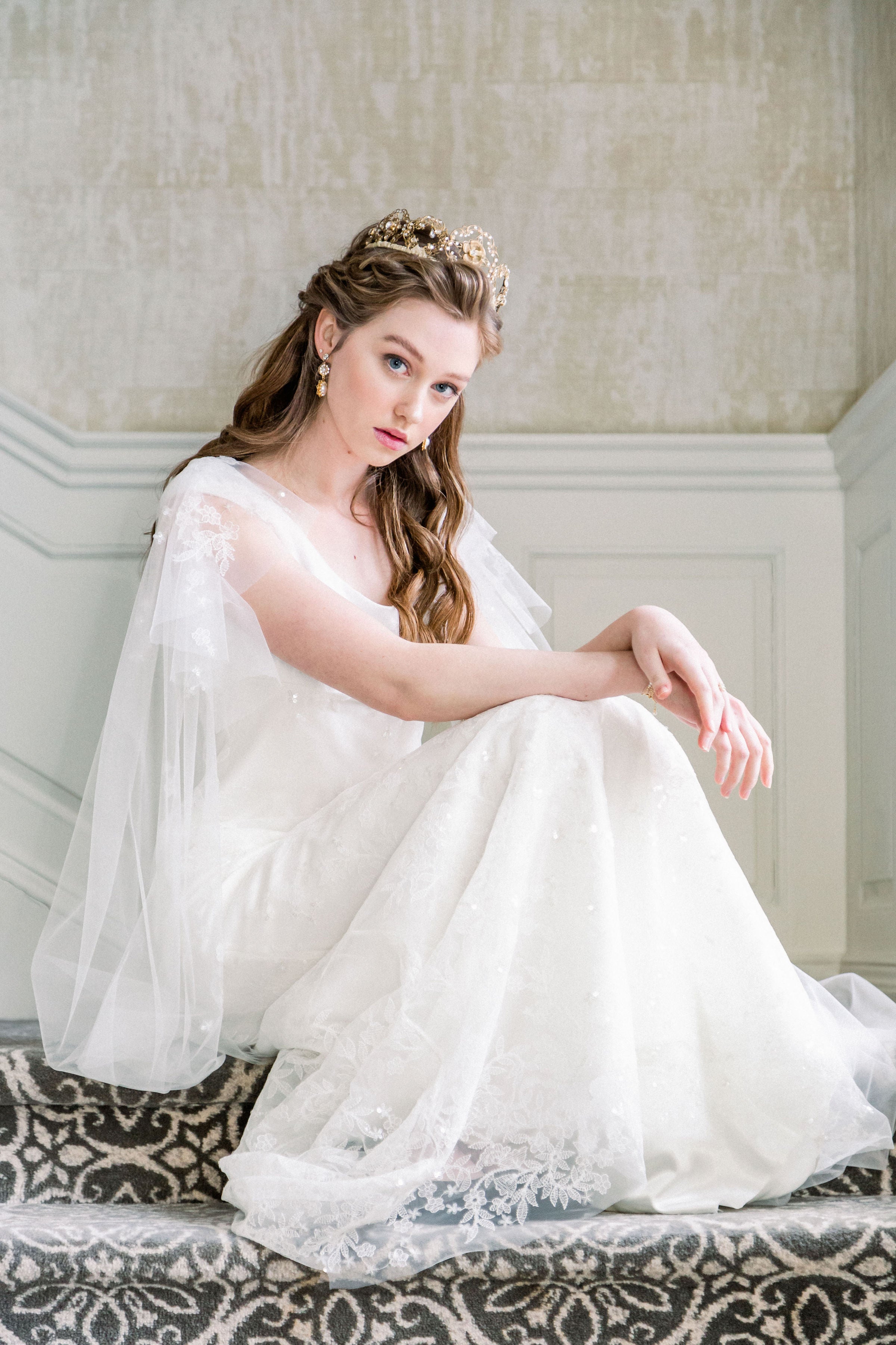 Woman in a white dress sitting on a patterned rug with a neutral wall background
