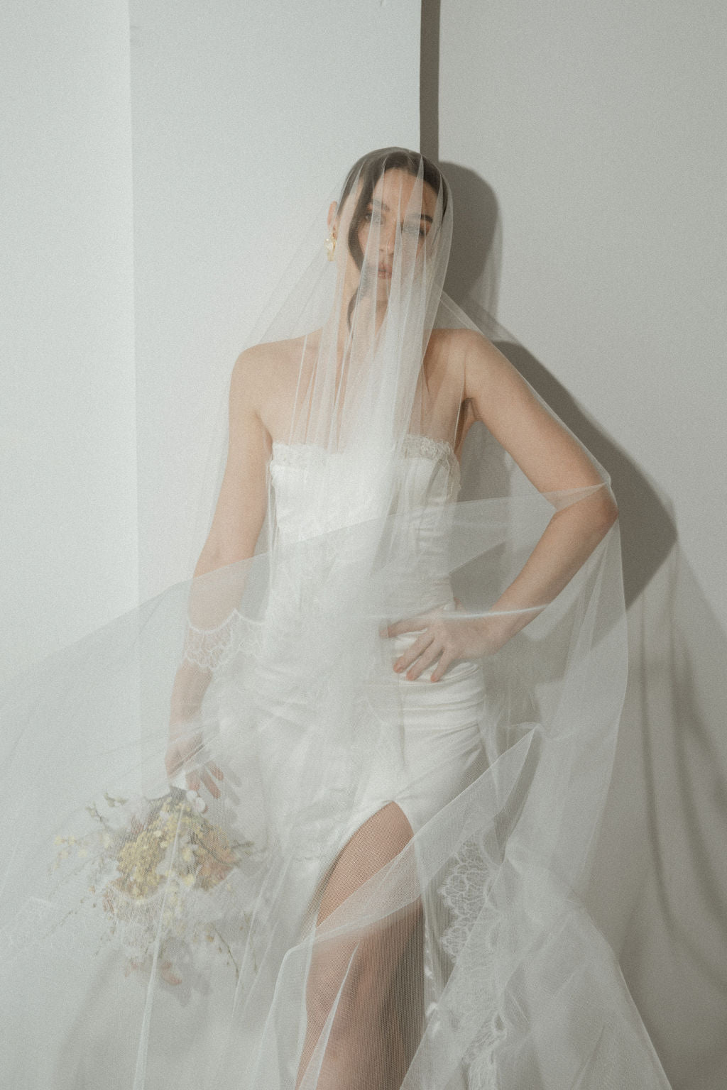 Woman in a white wedding dress with a long veil against a plain background