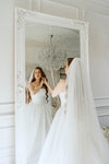 Bride in a white wedding dress standing in front of a large mirror, adjusting her veil.