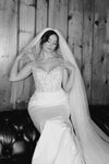 Black and white photo of a bride in a wedding dress with a veil against a wooden wall.