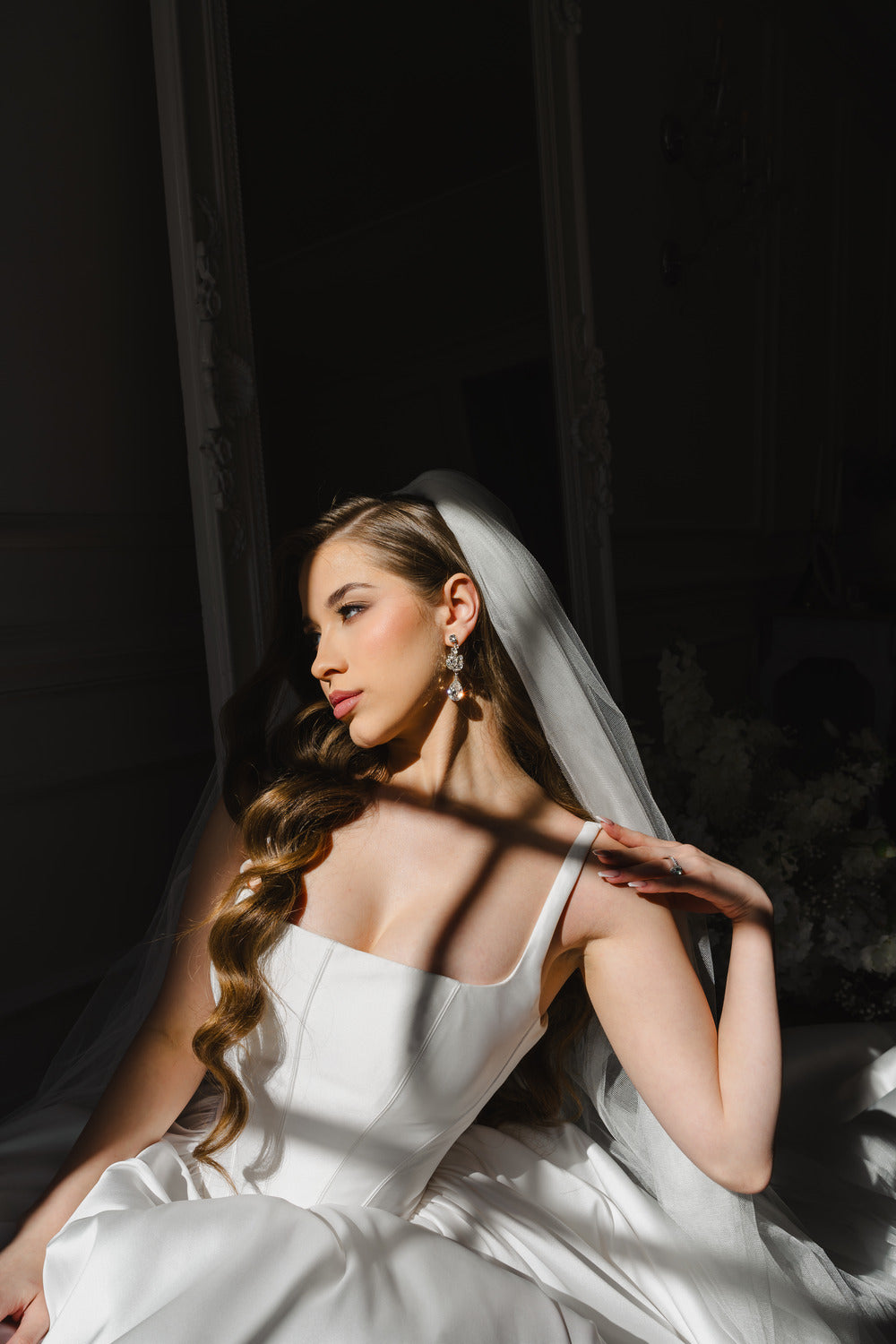 Bride in a white dress with a veil sitting against a dark background
