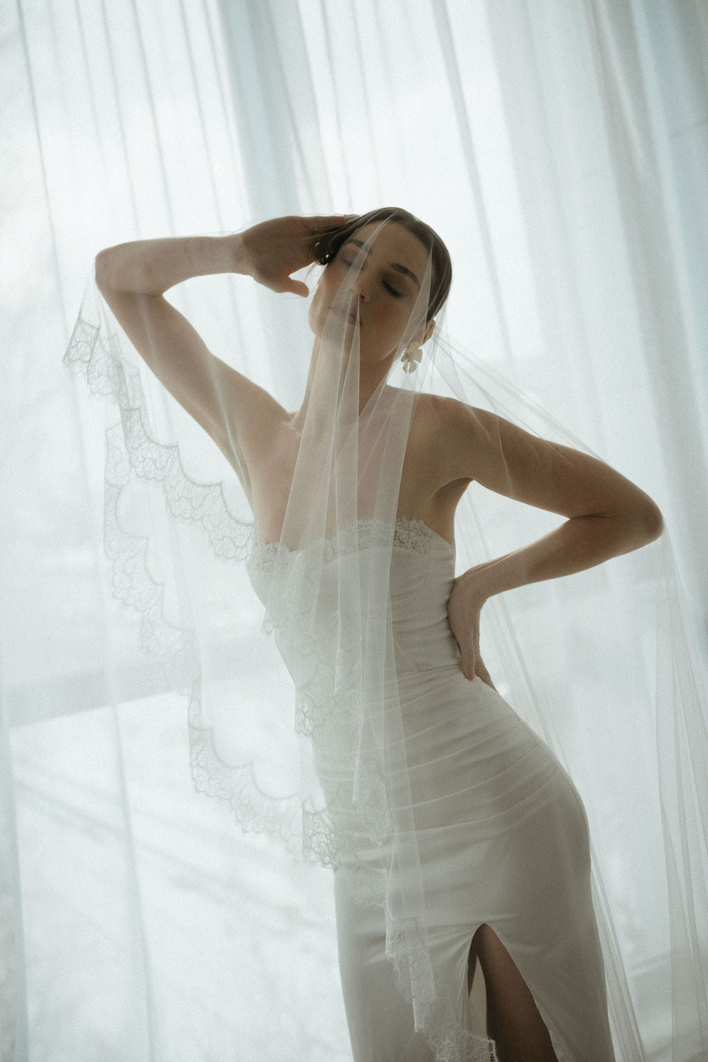 Woman in a white dress standing behind sheer curtains