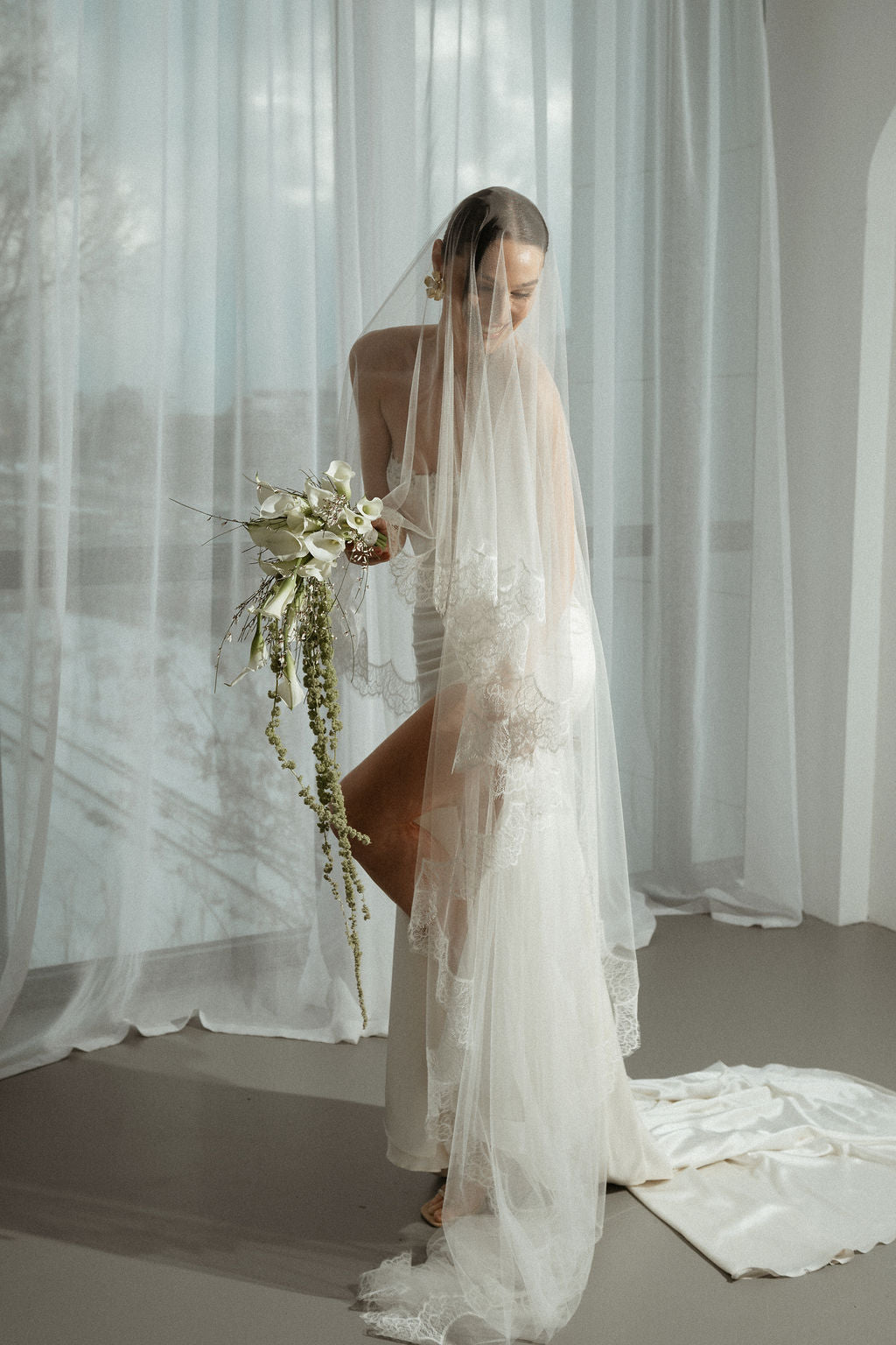Bride holding a bouquet in front of sheer curtains