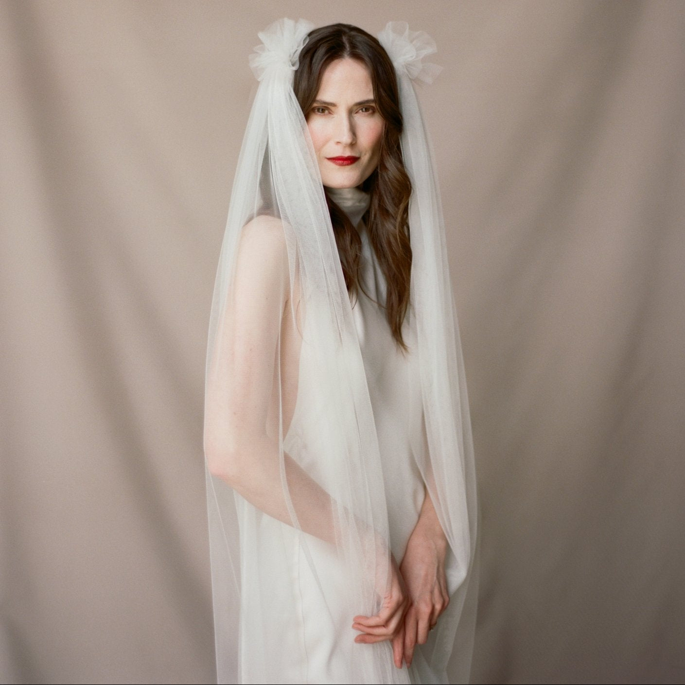 Woman wearing a white wedding dress with a veil against a beige background