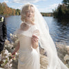 Bride with veil standing by a lake on a sunny day