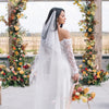 Bride in a white wedding dress with a long veil standing in front of floral arches.
