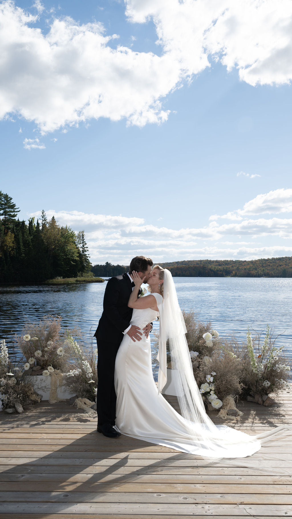 Couple kissing on a dock by a lake with a scenic background