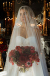 Bride holding a bouquet of red flowers with a blurred candlelit background