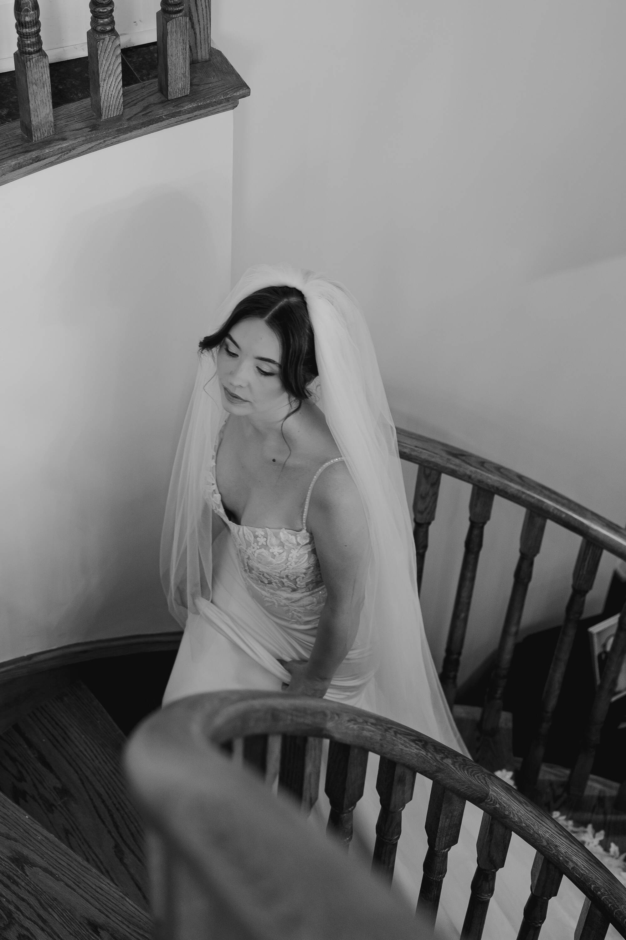 Black and white photo of a woman in a wedding dress with a veil on a staircase.