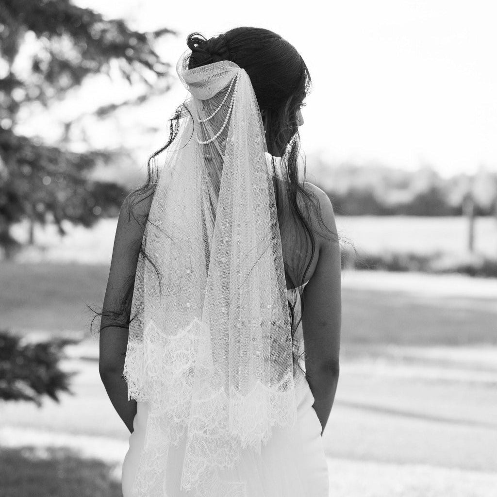 Black and white photo of a bride holding her veil outdoors.