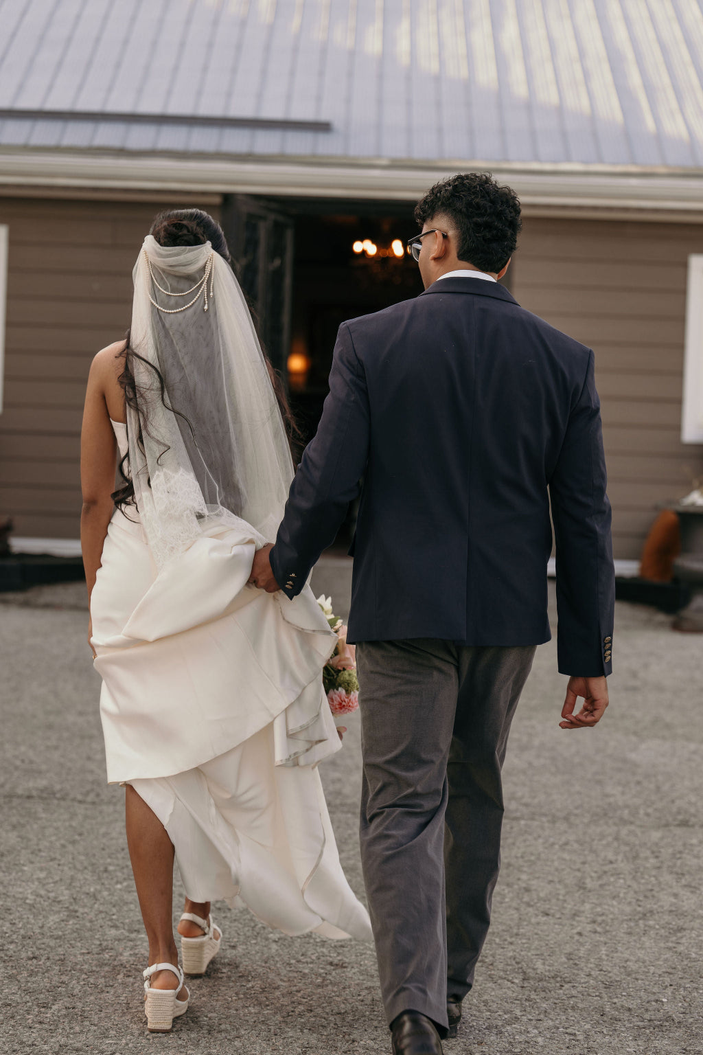 Man and woman holding hands, walking away from a building entrance.