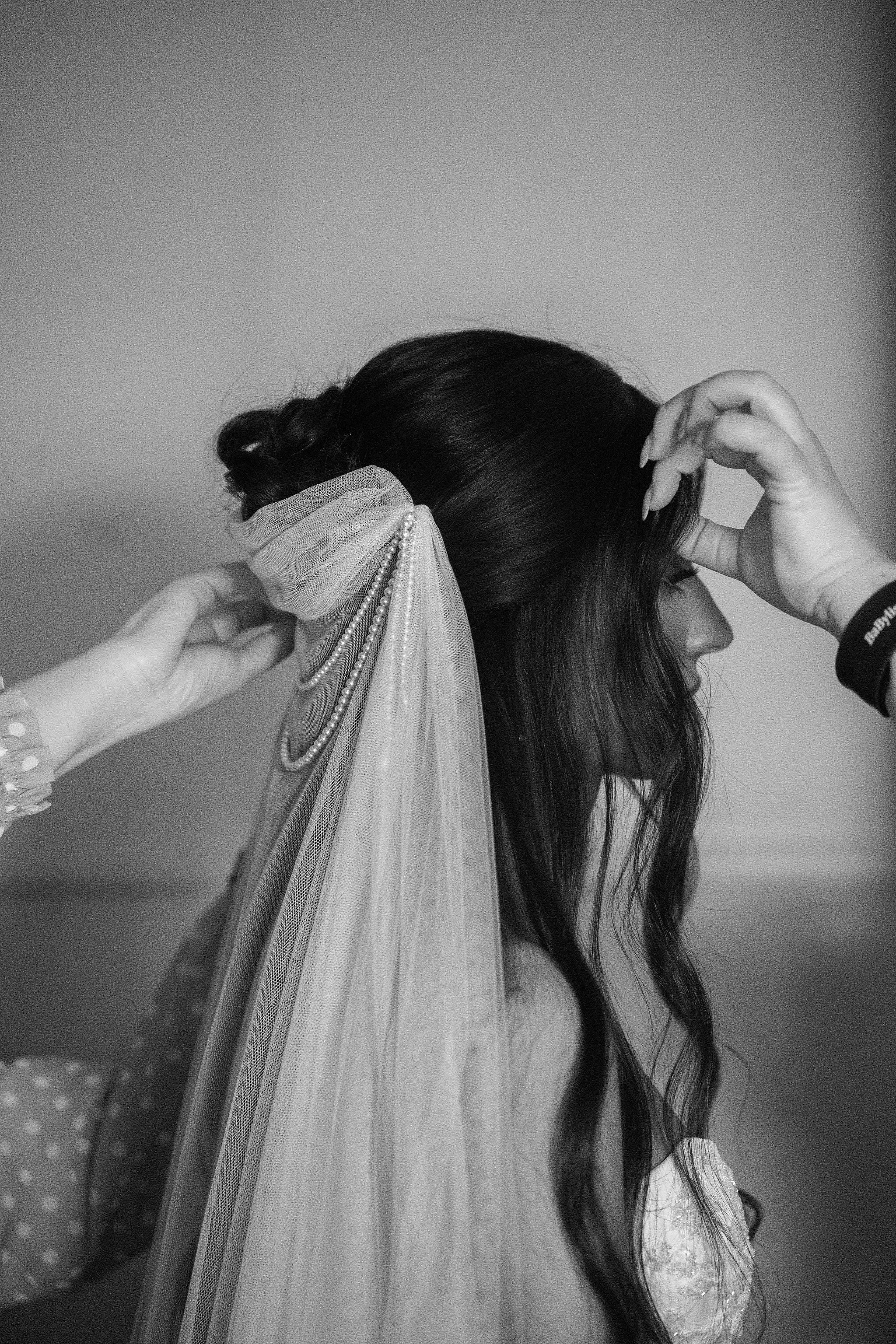 Person adjusting a veil on another person's head, with a neutral background