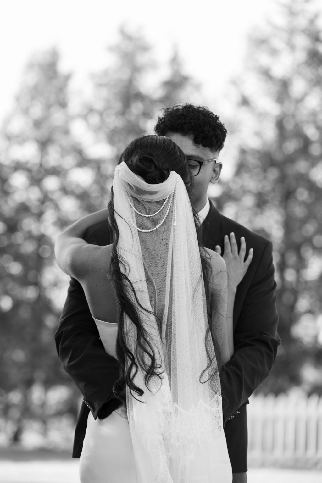 Black and white photo of a couple embracing outdoors with trees in the background