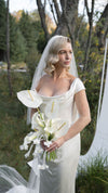 Woman in a white wedding dress holding a bouquet outdoors with trees in the background