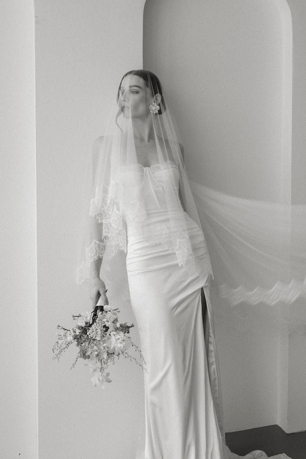 Bride in a white wedding dress with a long veil against a plain background