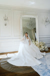 Woman in a white wedding dress standing in front of a large mirror in a elegant room.