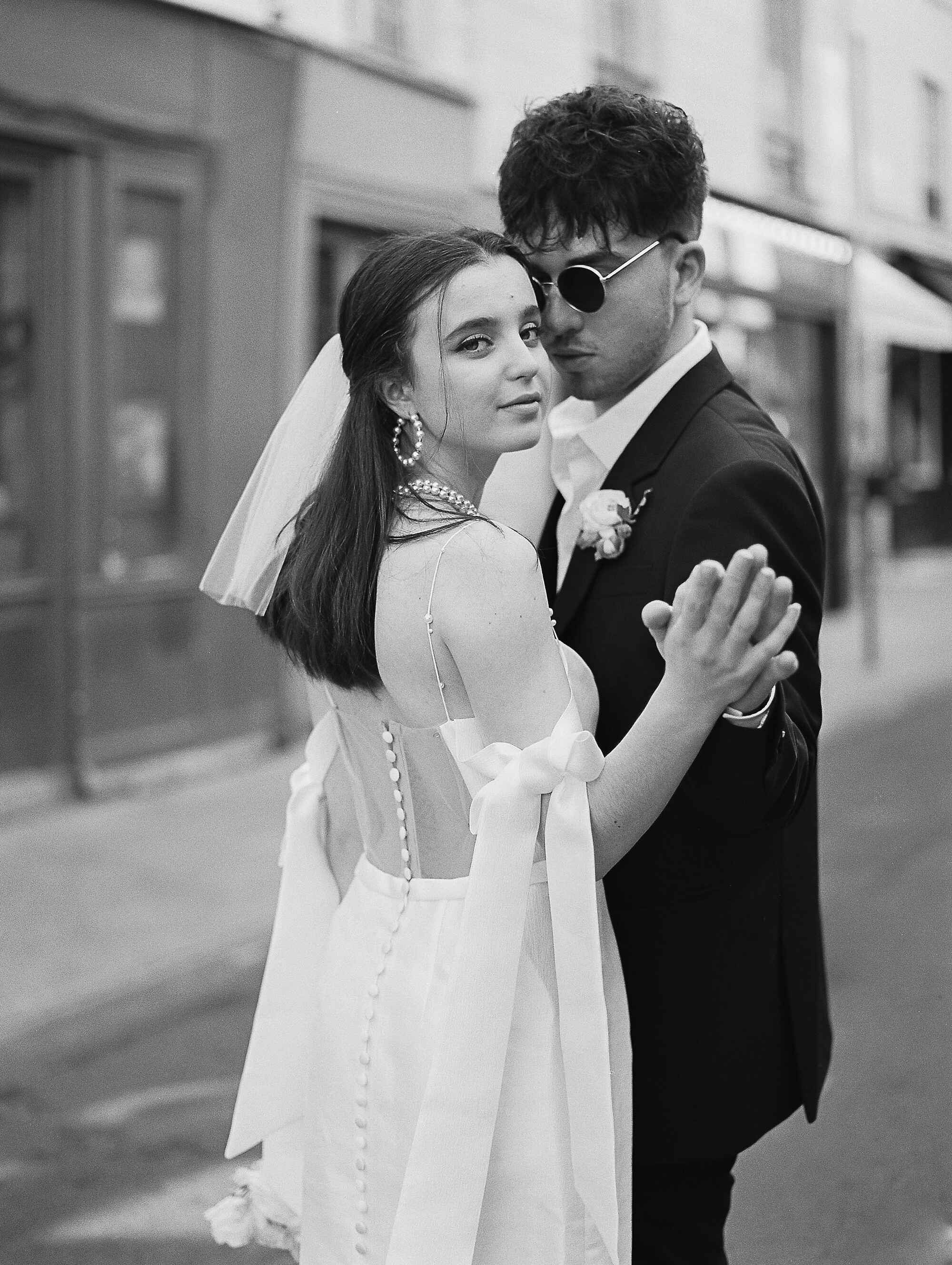 Black and white photo of a couple in formal attire on a city street.