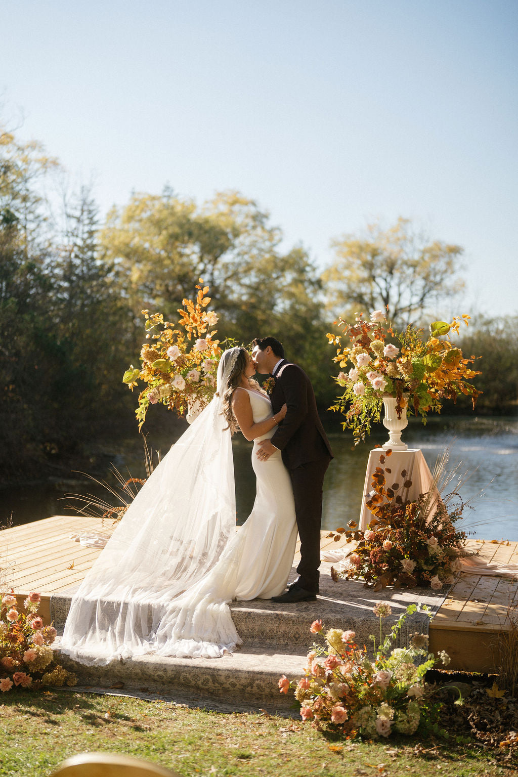 Couple embracing on a dock with floral arrangements and a lake in the background