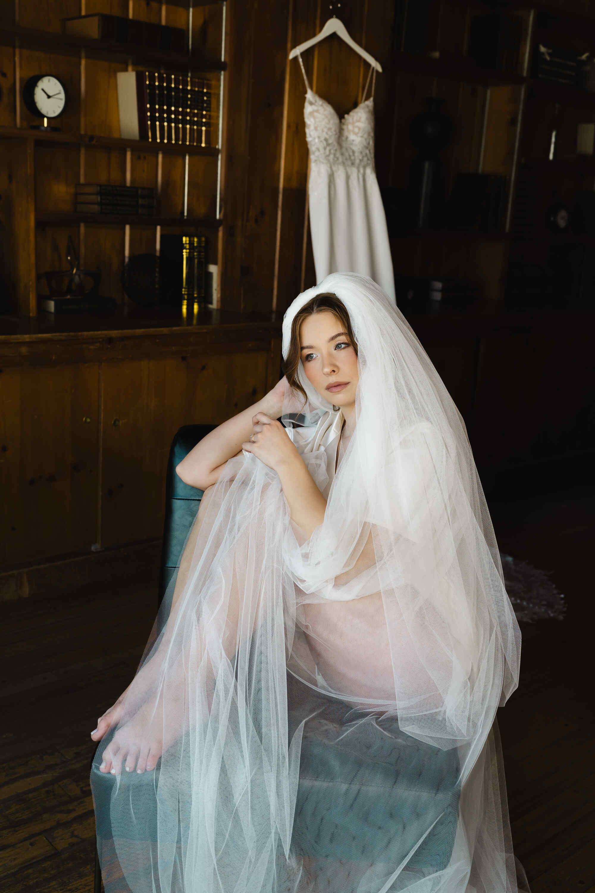 Woman in a wedding dress with a veil sitting in a room with wooden walls.
