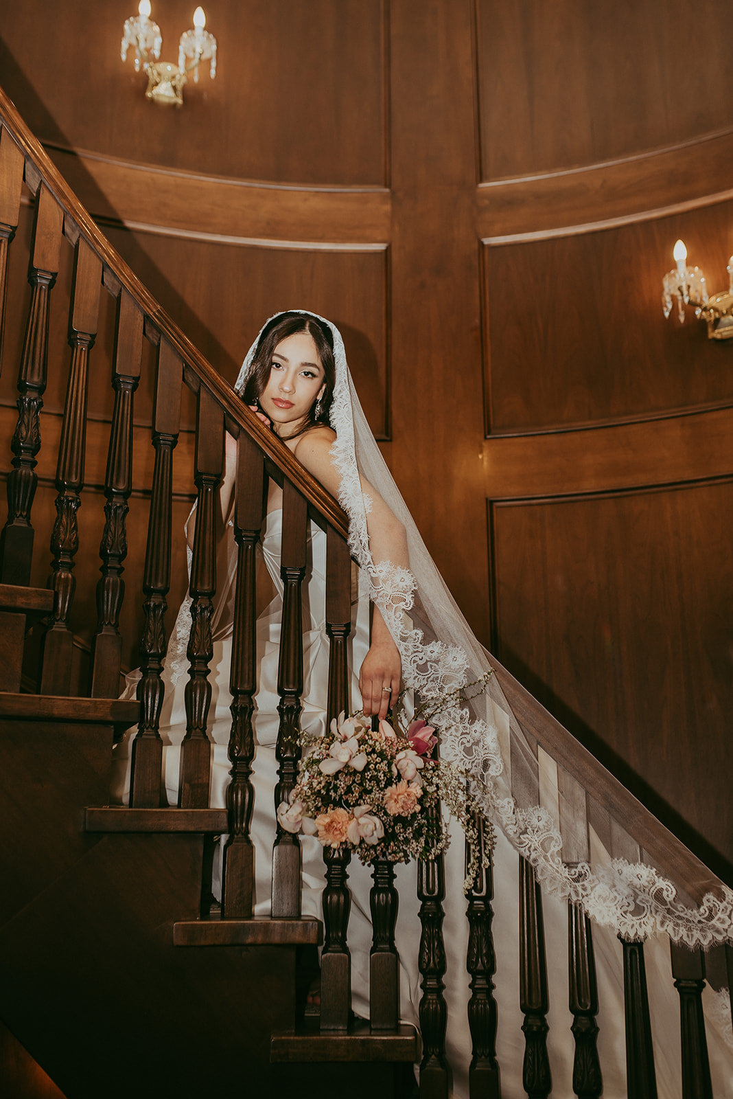 Woman in a wedding dress with a long veil standing on a wooden staircase.