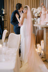 Couple embracing in a wedding setting with a decorated table and cake.