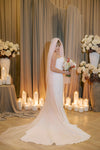 Bride in a white gown holding flowers in a decorated room with candles and floral arrangements.
