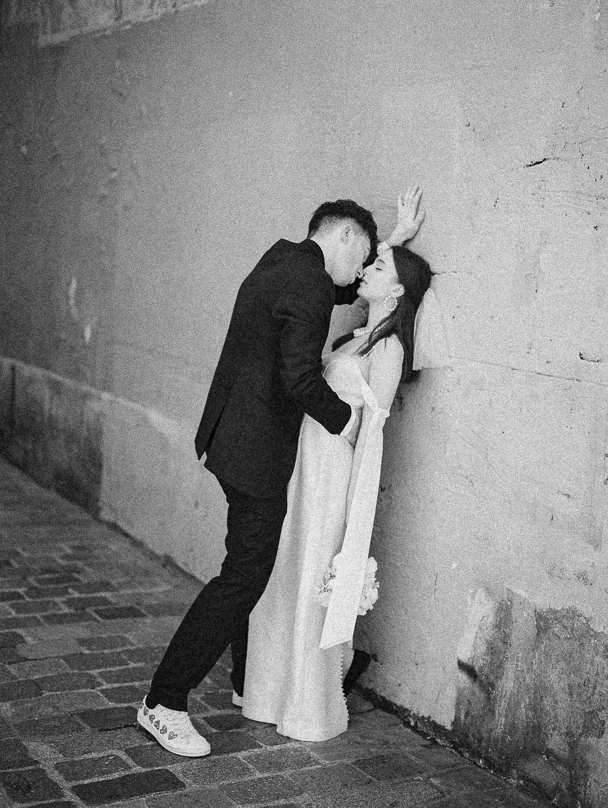 Black and white photo of a couple embracing against a wall.
